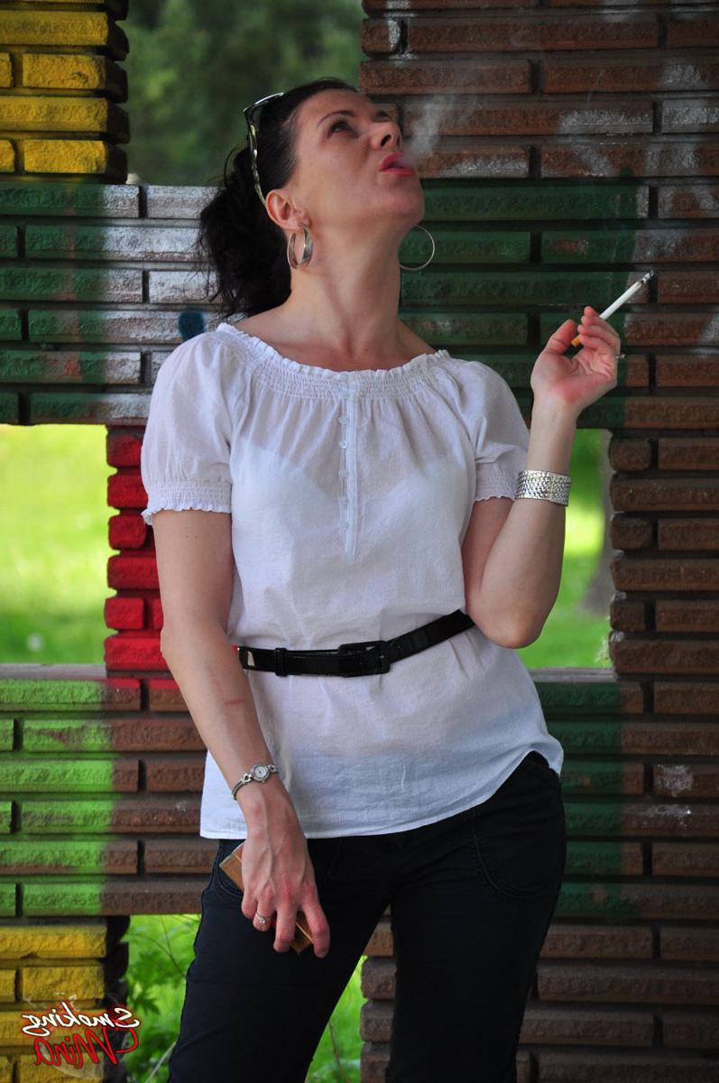 15P Fully clothed brunette Mina smokes a cigarette in front of a brick wall