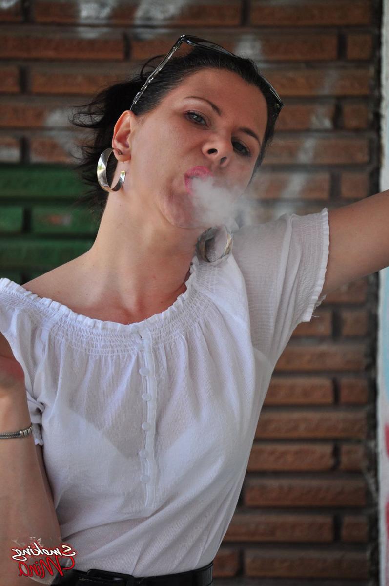 15P Fully clothed brunette Mina smokes a cigarette in front of a brick wall