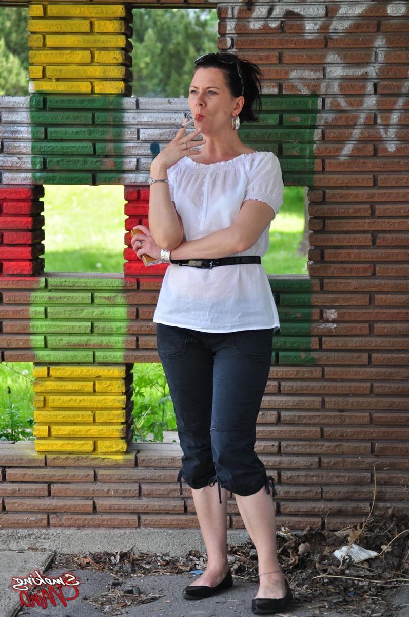 15P Fully clothed brunette Mina smokes a cigarette in front of a brick wall