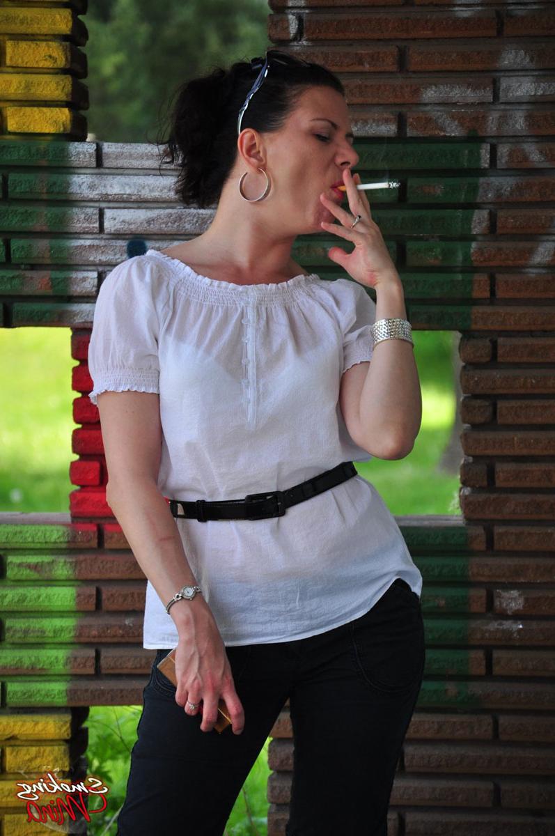 15P Fully clothed brunette Mina smokes a cigarette in front of a brick wall