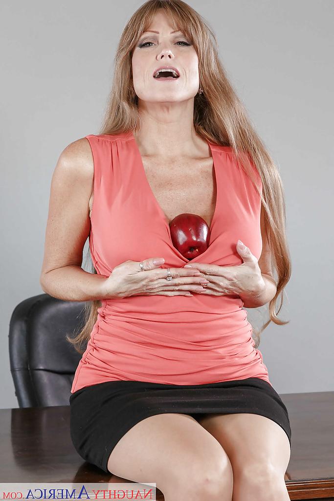 16P Darla Crane, enseignante mature, montre ses gros seins sur son bureau et porte des bas marron clair.