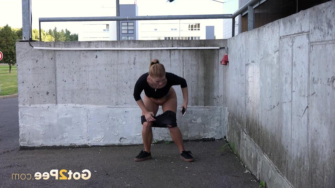 15P Chrissy, une femme vêtue, s'accroupit pour pisser dans un lieu public.