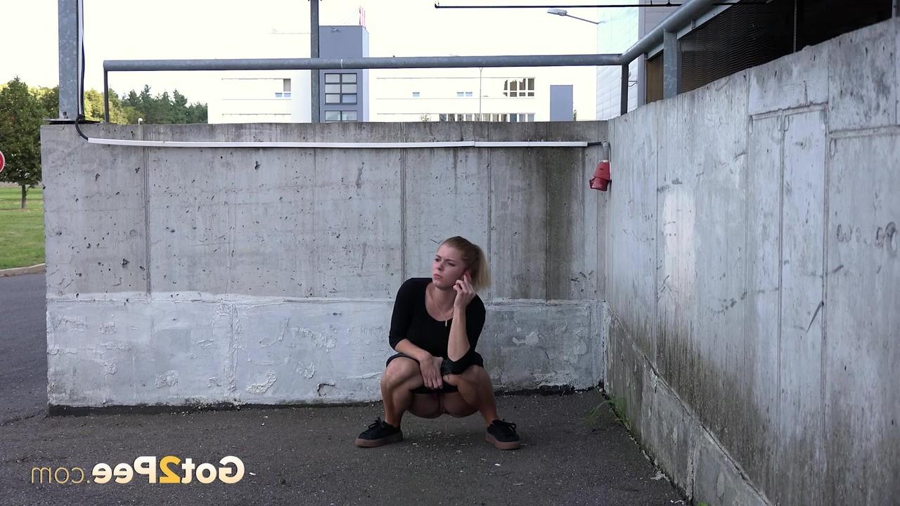 15P Chrissy, une femme vêtue, s'accroupit pour pisser dans un lieu public.