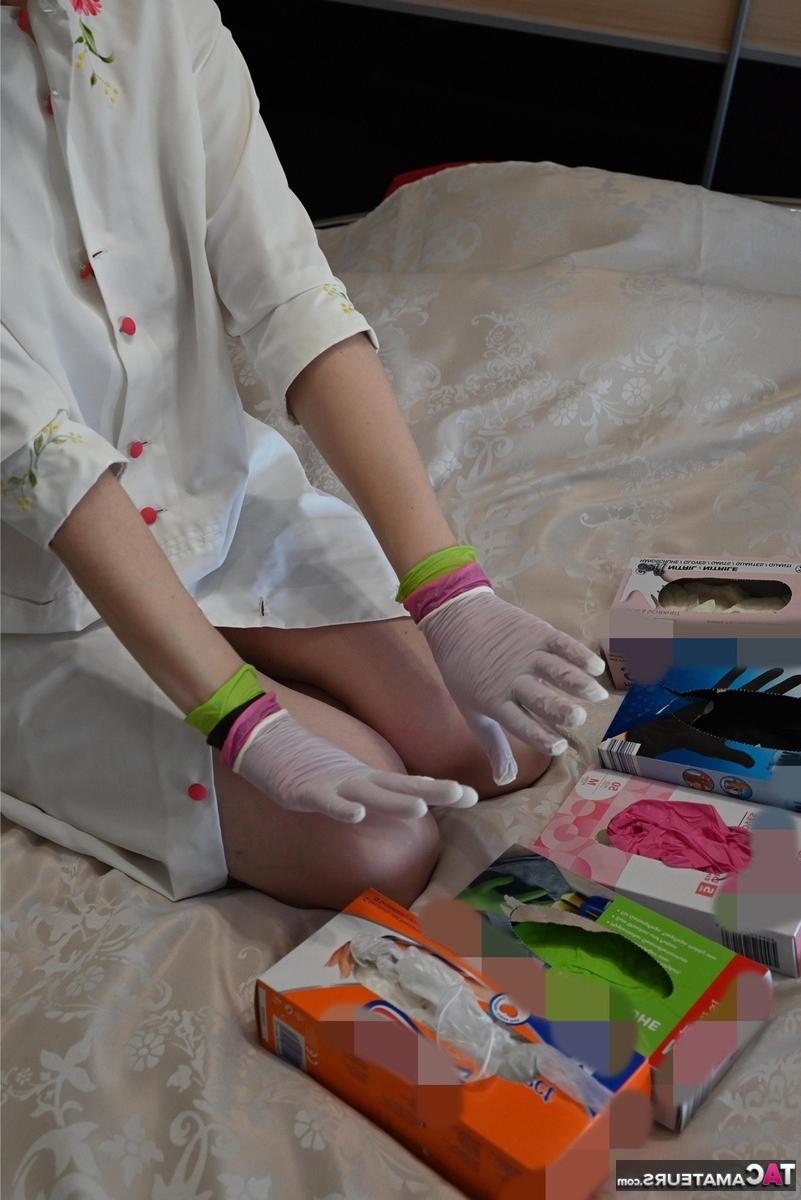 16P Amateurfrau kniet auf ihrem Bett und zieht Schichten von Latexhandschuhen an