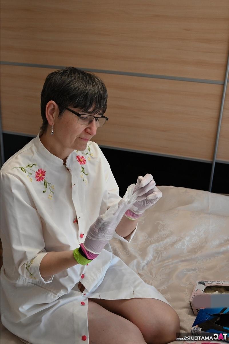 16P Amateurfrau kniet auf ihrem Bett und zieht Schichten von Latexhandschuhen an