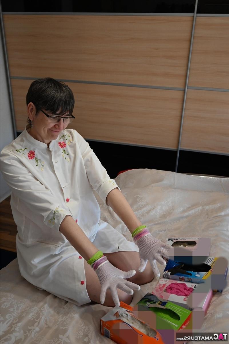 16P Amateurfrau kniet auf ihrem Bett und zieht Schichten von Latexhandschuhen an