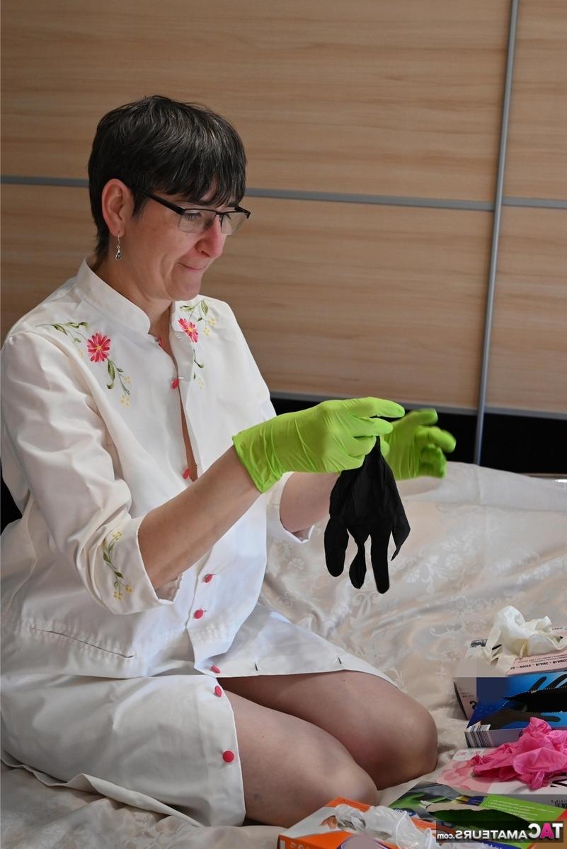 16P Amateurfrau kniet auf ihrem Bett und zieht Schichten von Latexhandschuhen an