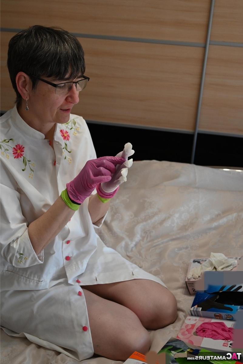 16P Amateurfrau kniet auf ihrem Bett und zieht Schichten von Latexhandschuhen an
