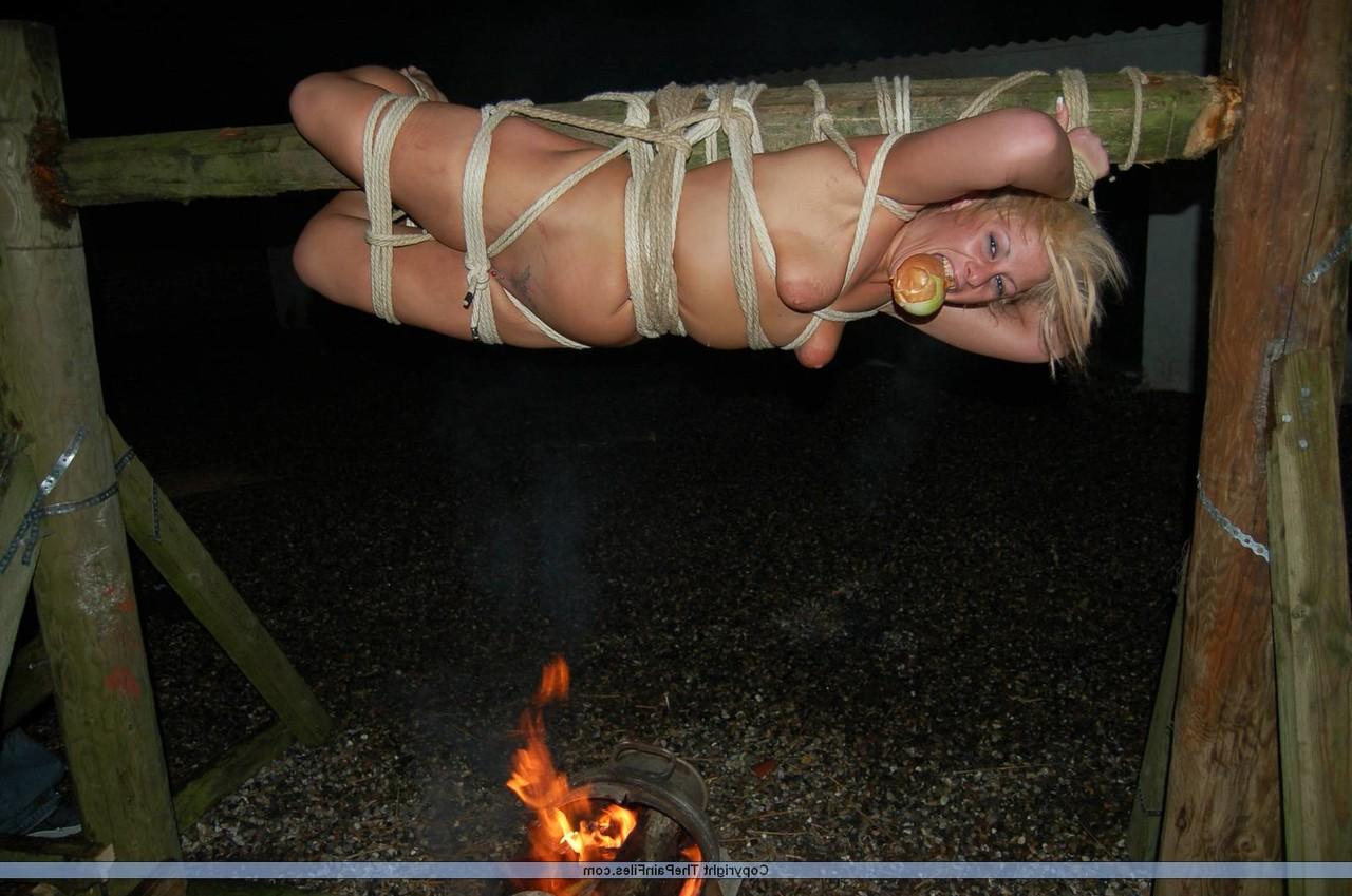 16P Rubia desnuda con una manzana en la boca es asada al fuego mientras está atada con una cuerda