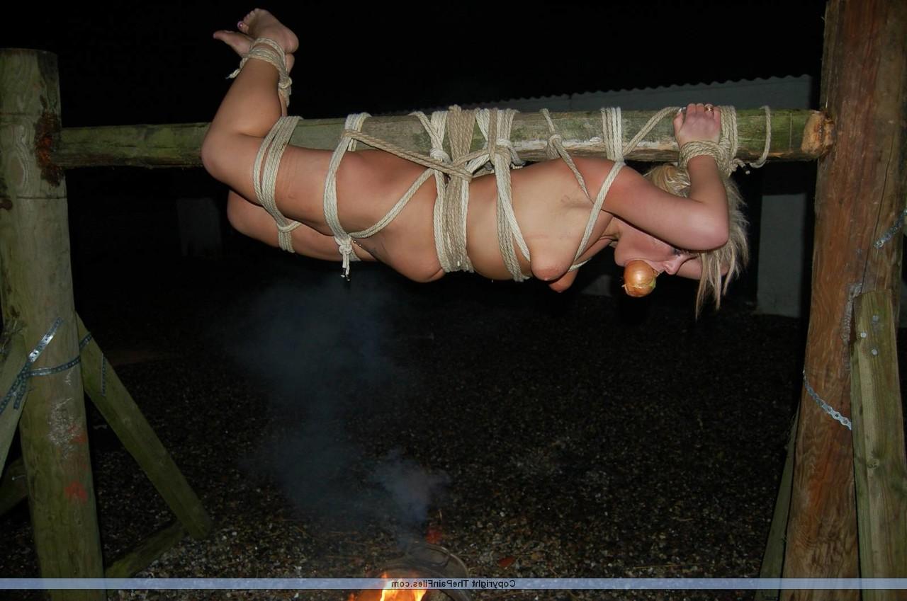 16P Rubia desnuda con una manzana en la boca es asada al fuego mientras está atada con una cuerda