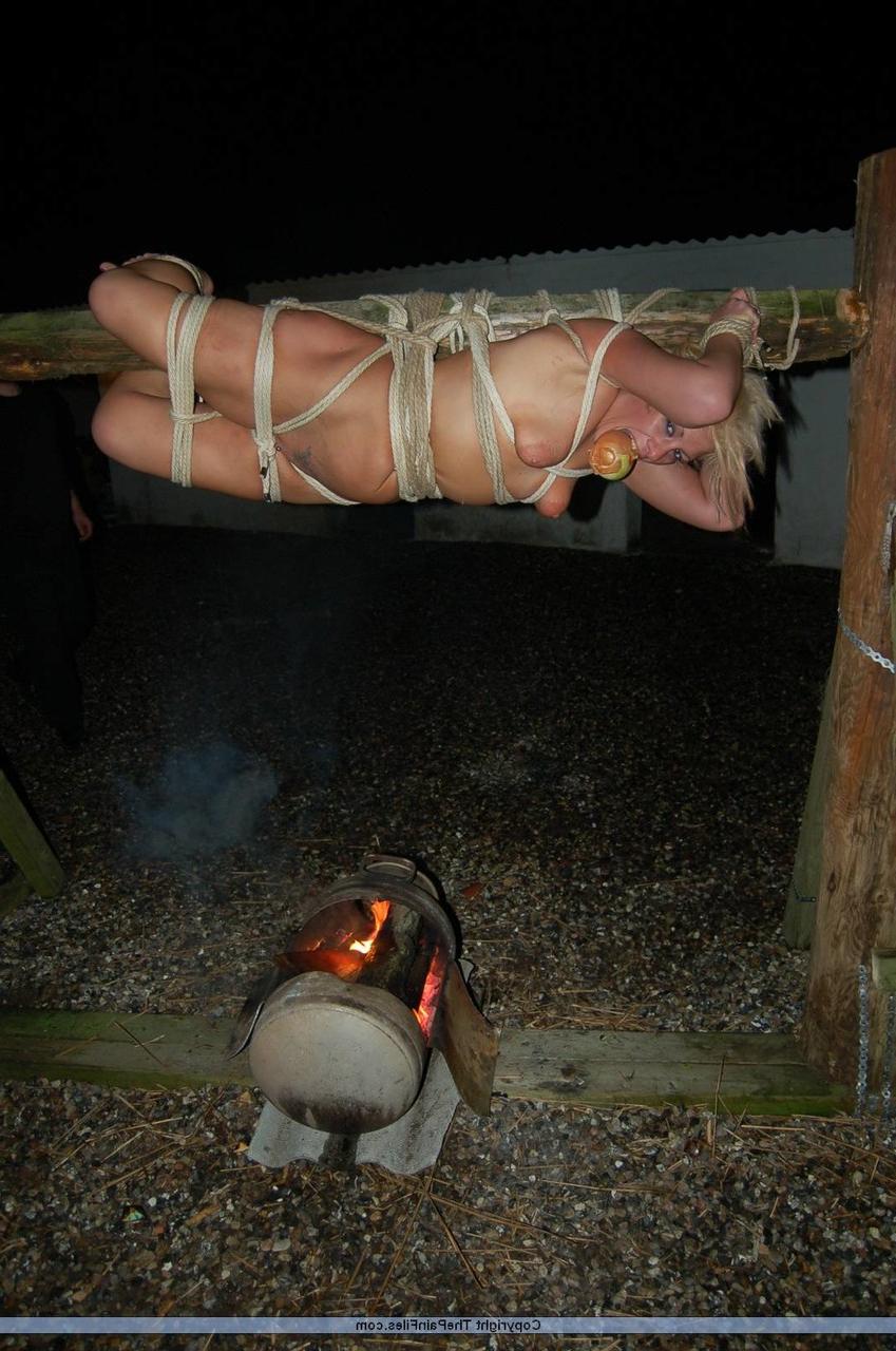 16P Rubia desnuda con una manzana en la boca es asada al fuego mientras está atada con una cuerda