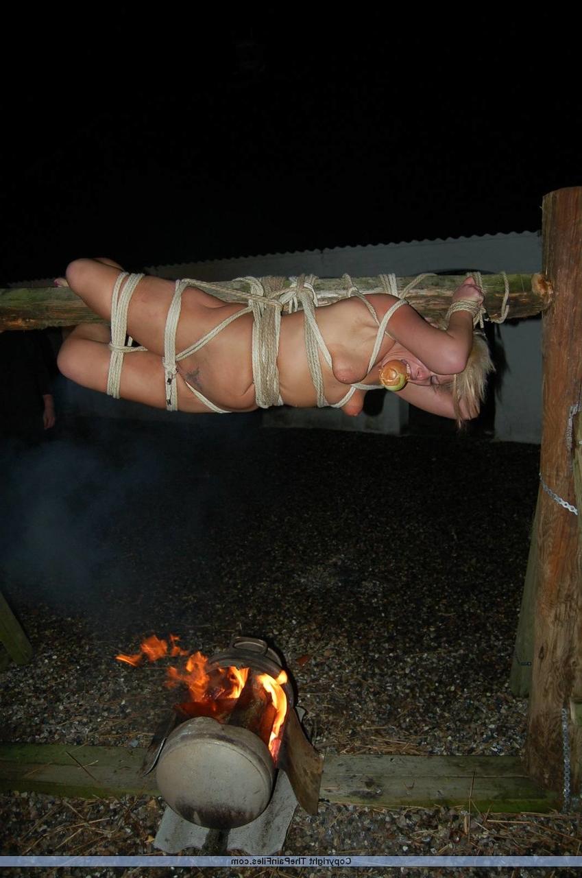 16P Rubia desnuda con una manzana en la boca es asada al fuego mientras está atada con una cuerda