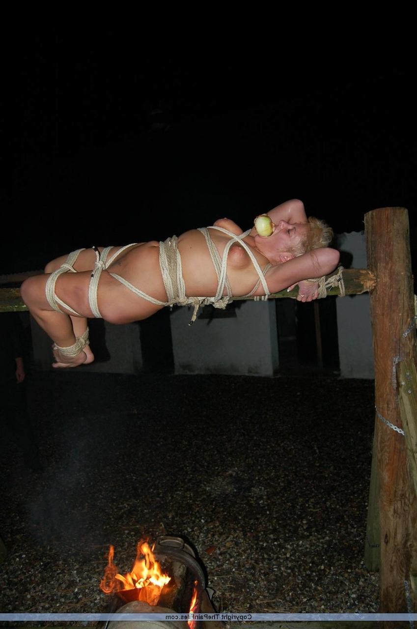 16P Rubia desnuda con una manzana en la boca es asada al fuego mientras está atada con una cuerda