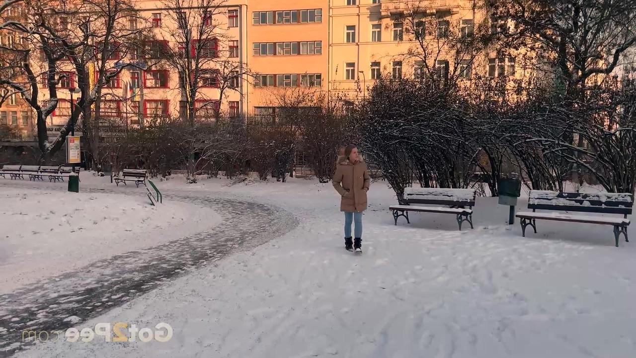 15P A simpática garota Juliia abaixa as calças para fazer xixi no chão coberto de neve em um parque