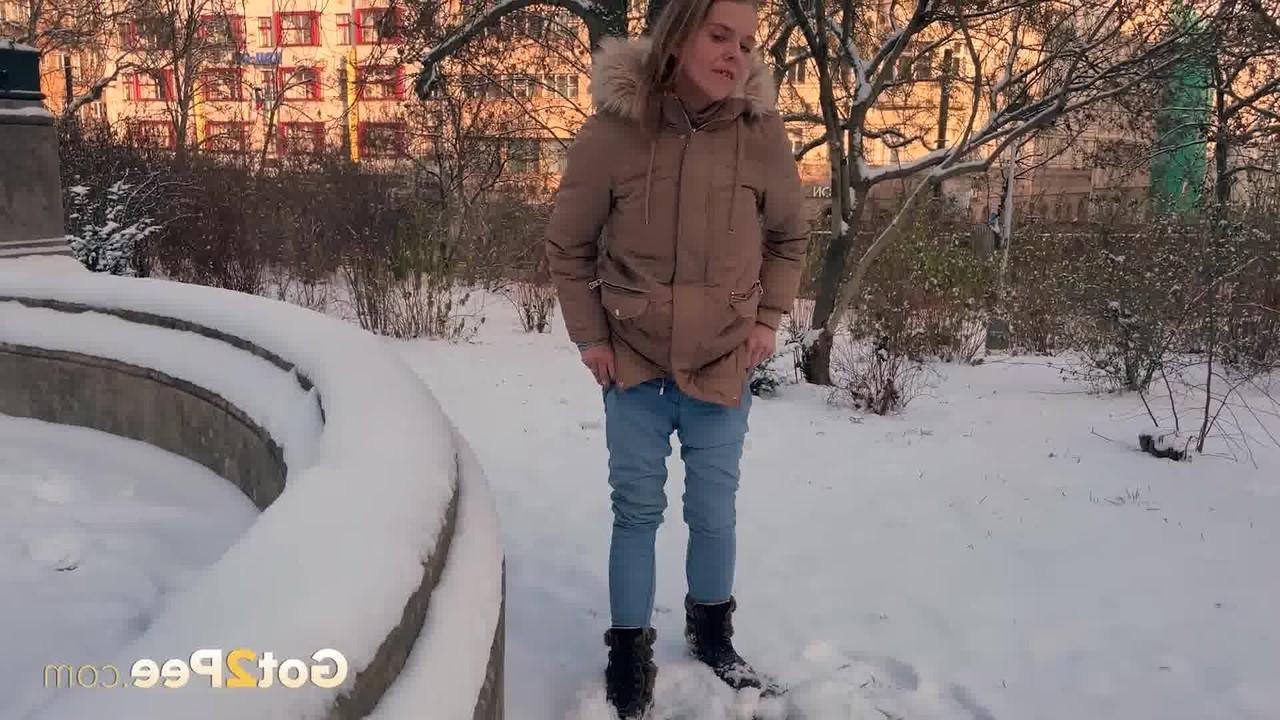 15P A simpática garota Juliia abaixa as calças para fazer xixi no chão coberto de neve em um parque