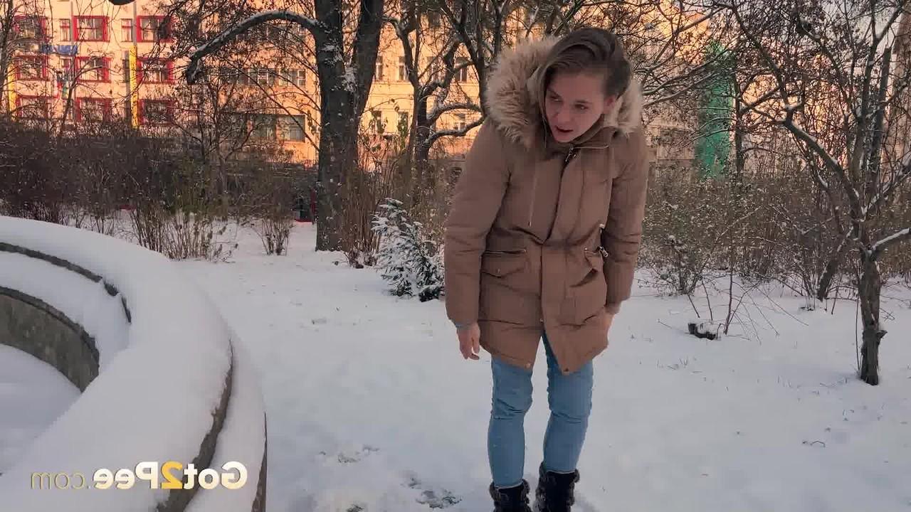 15P A simpática garota Juliia abaixa as calças para fazer xixi no chão coberto de neve em um parque