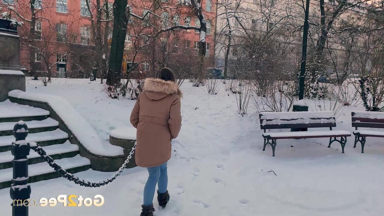 15P A simpática garota Juliia abaixa as calças para fazer xixi no chão coberto de neve em um parque