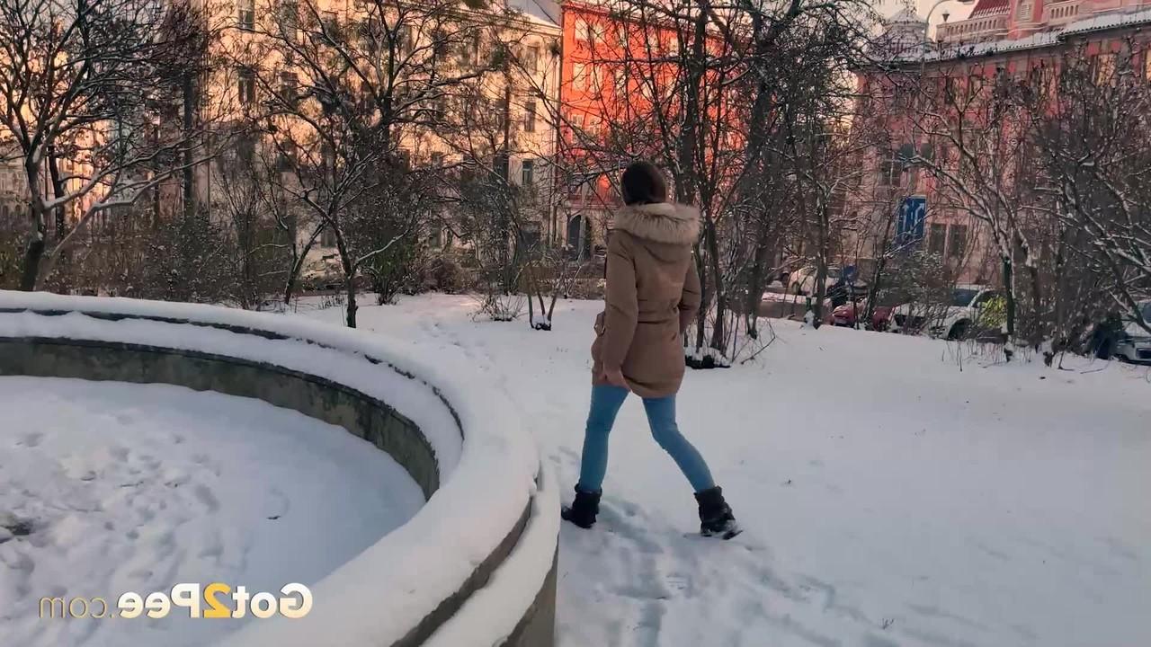 15P A simpática garota Juliia abaixa as calças para fazer xixi no chão coberto de neve em um parque