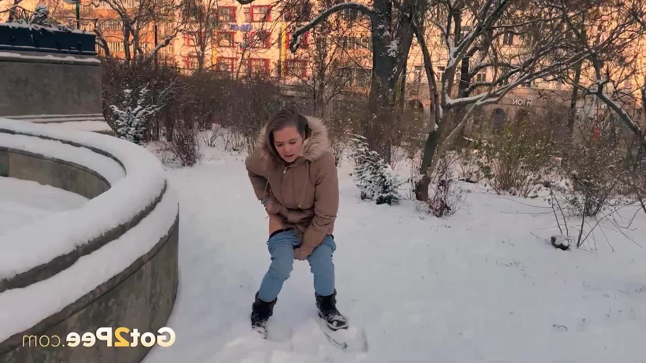 15P A simpática garota Juliia abaixa as calças para fazer xixi no chão coberto de neve em um parque
