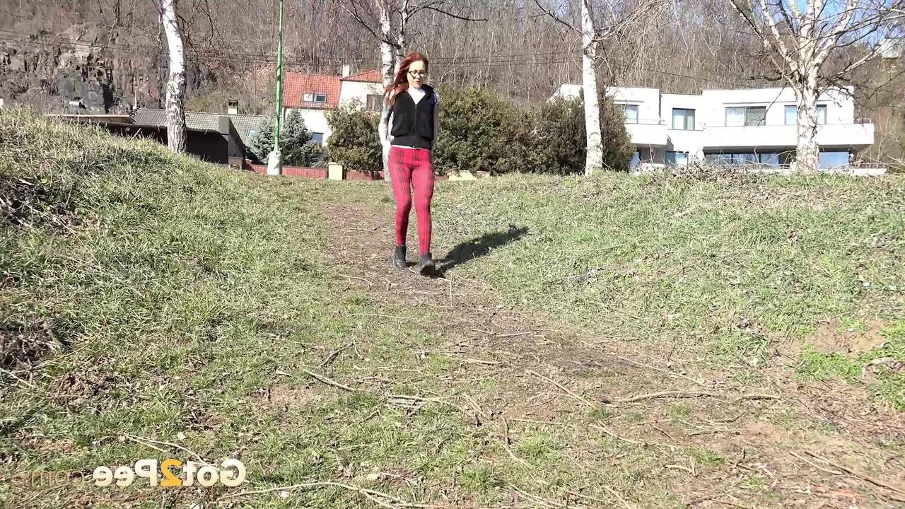 15P Redheaded girl Sandra pees on a path while walking near the water