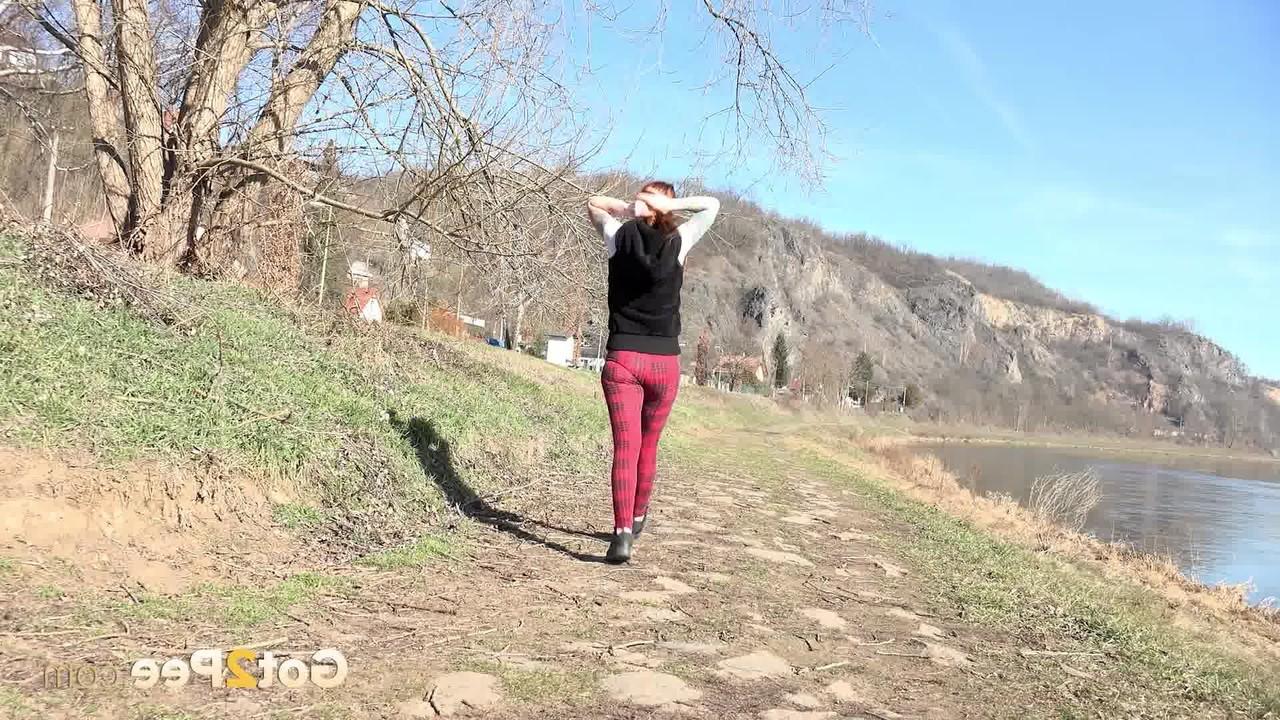 15P Redheaded girl Sandra pees on a path while walking near the water