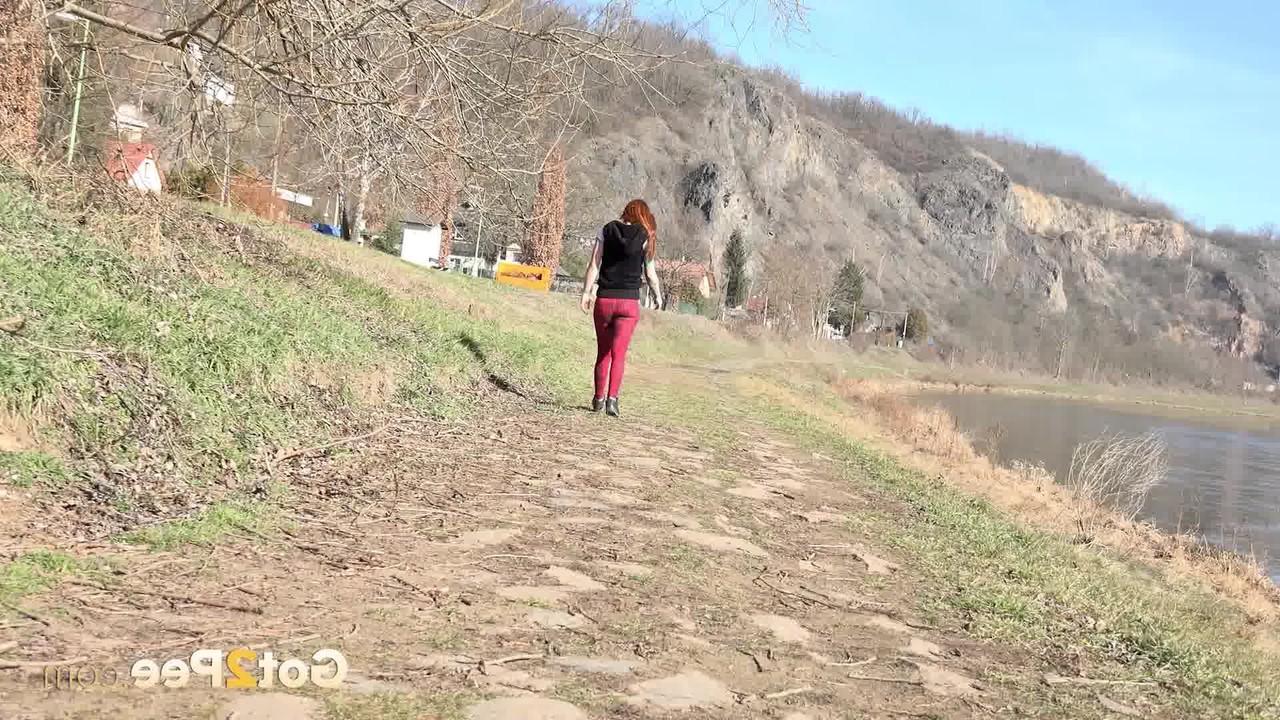 15P Redheaded girl Sandra pees on a path while walking near the water