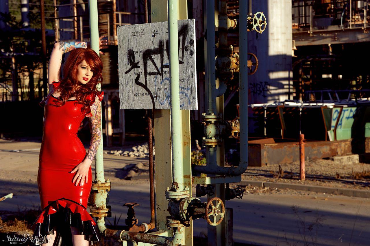 12P La chaude rousse Vanessa Lake enlève une robe en latex pour se mettre nue sur des marches rouillées.