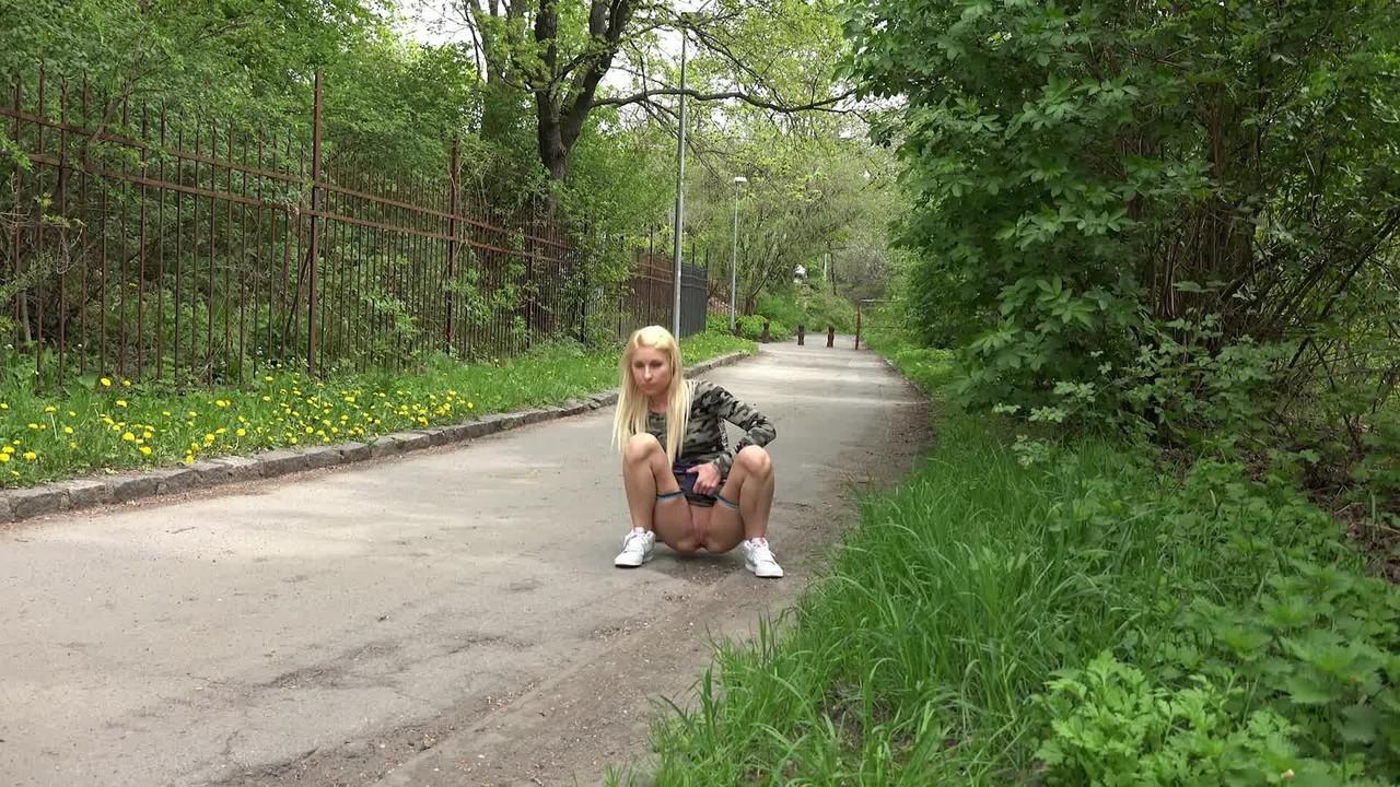 15P Nykla, une fille blanche aux cheveux blonds, pisse sur une route pavée.