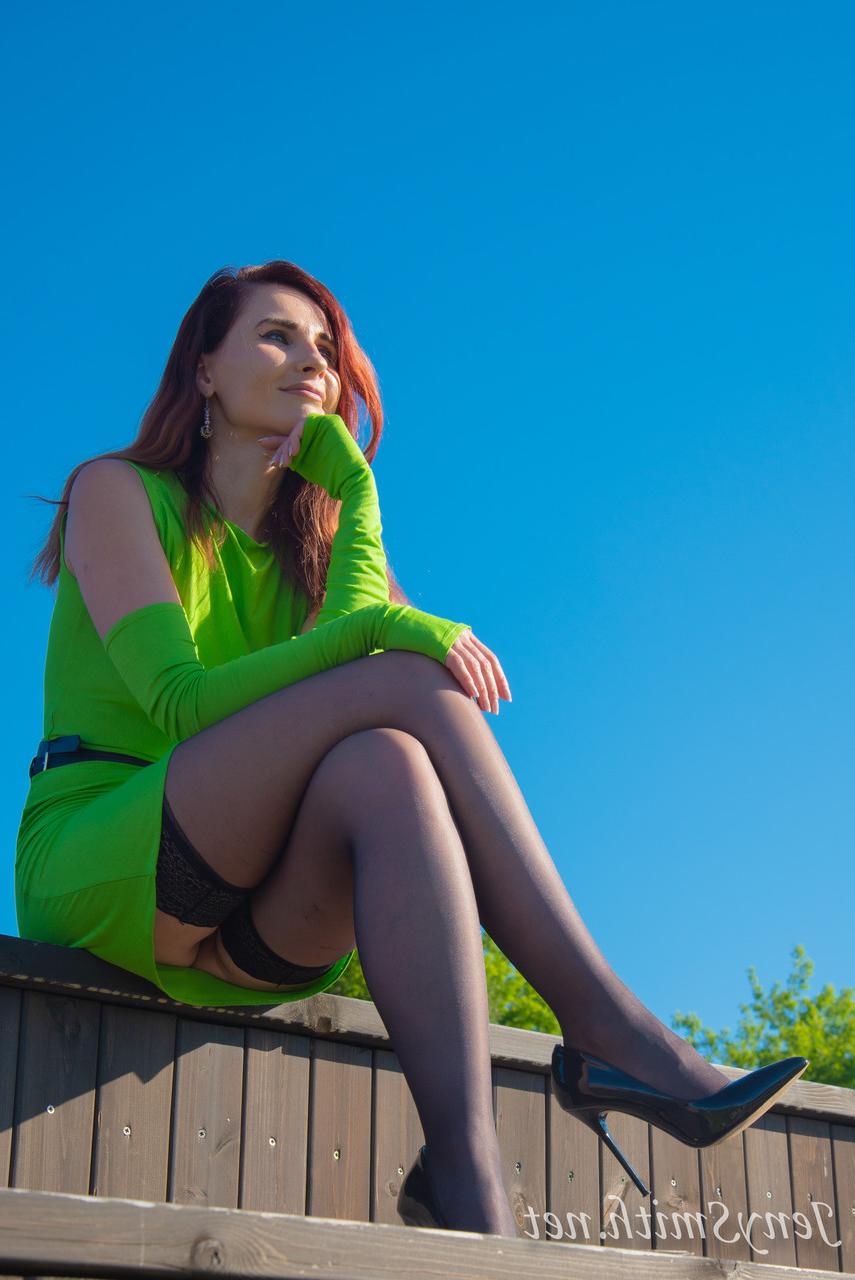 15P Jeny Smith, une fille mince vêtue d'une robe verte, montre ses fesses et pose en plein air.