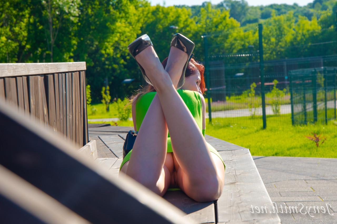 15P Jeny Smith, une fille mince vêtue d'une robe verte, montre ses fesses et pose en plein air.