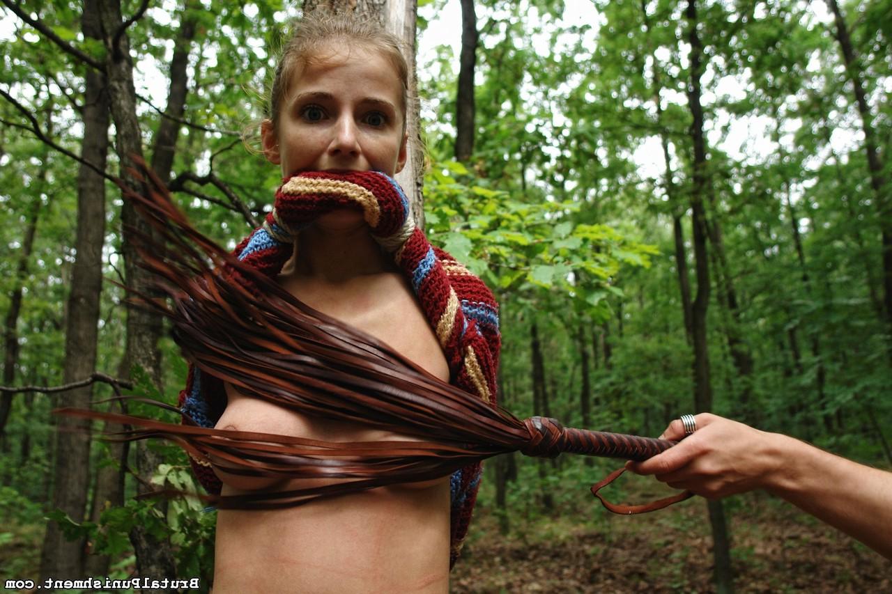 15P Petite blonde girl is flogged while tied to a tree in the forest