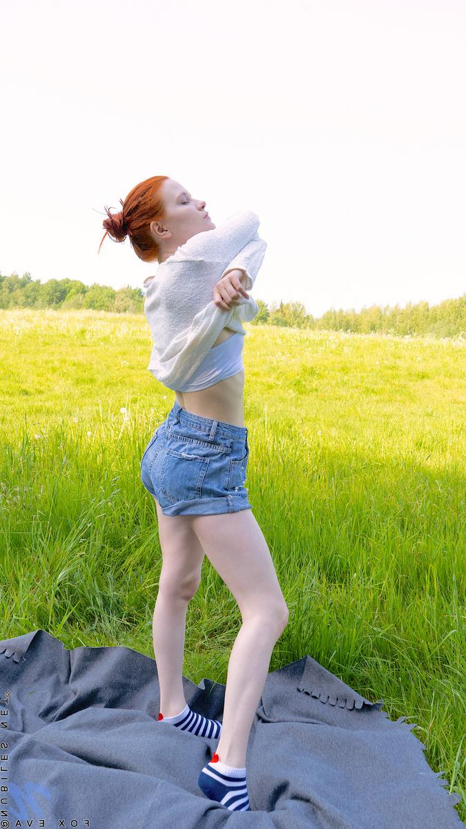 16P Fox Eva, jeune rousse et pâle, se met nue sur une couverture dans un champ.