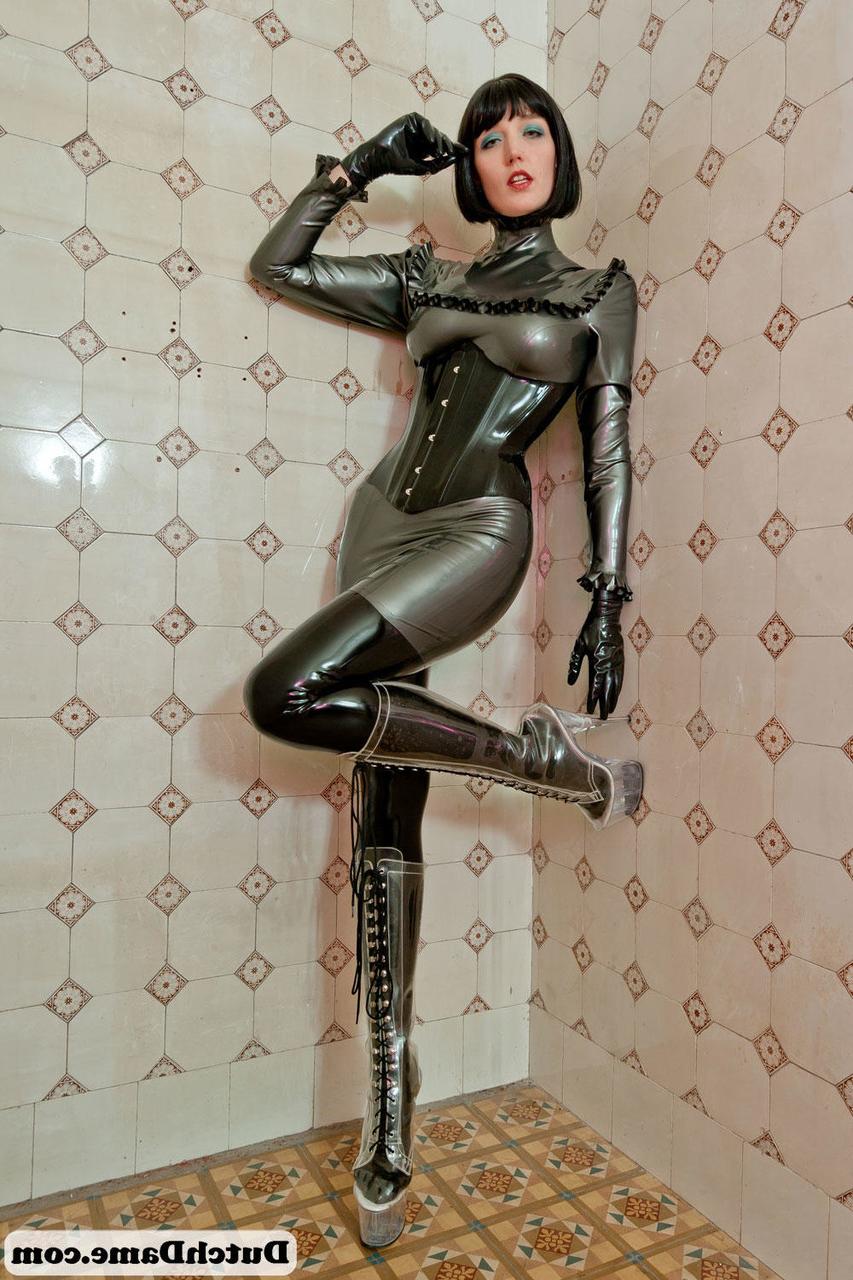 16P Mujer de cabello oscuro se pone faja sobre ropa de látex y botas