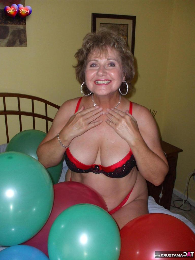 20P Busty Bliss, femme mûre, se met seins nus sur son lit en jouant avec des ballons.