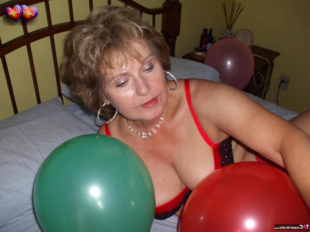 20P Busty Bliss, femme mûre, se met seins nus sur son lit en jouant avec des ballons.