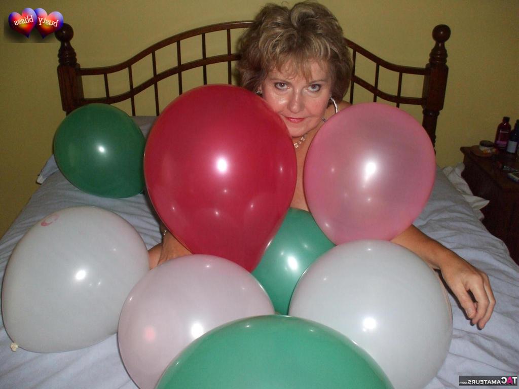 20P Busty Bliss, femme mûre, se met seins nus sur son lit en jouant avec des ballons.