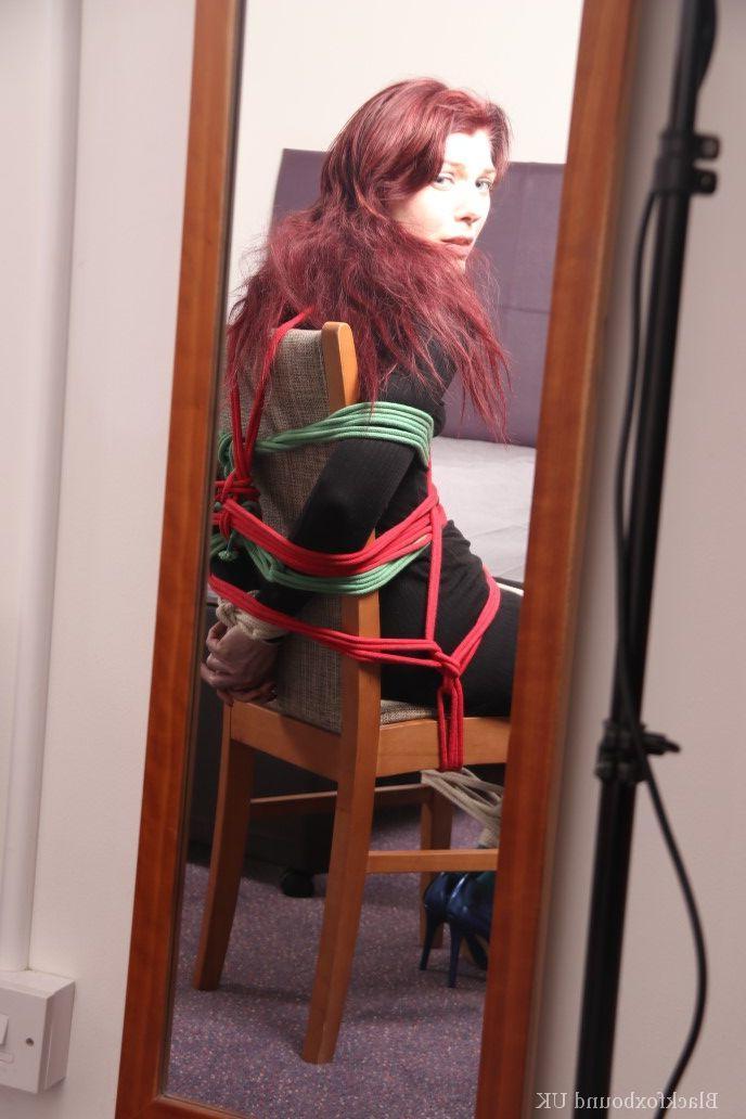 16P Menina branca com cabelo canela está amarrada a uma cadeira com um vestido escuro e meia azul
