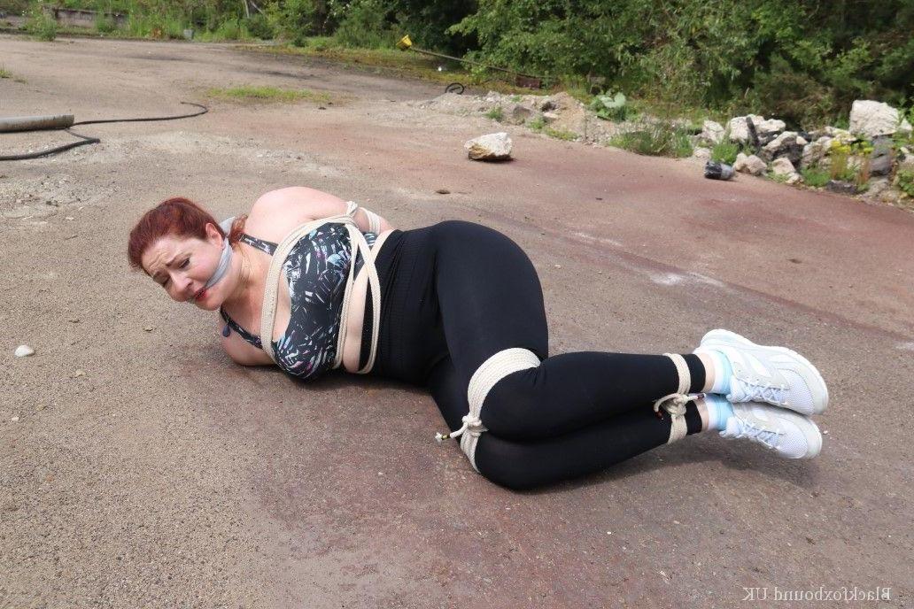 16P Redheaded girl Mada Rose is left on a paved lot while tied up