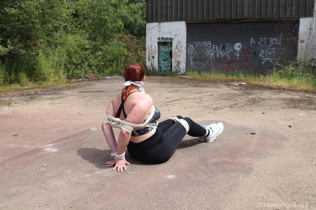 16P Redheaded girl Mada Rose is left on a paved lot while tied up