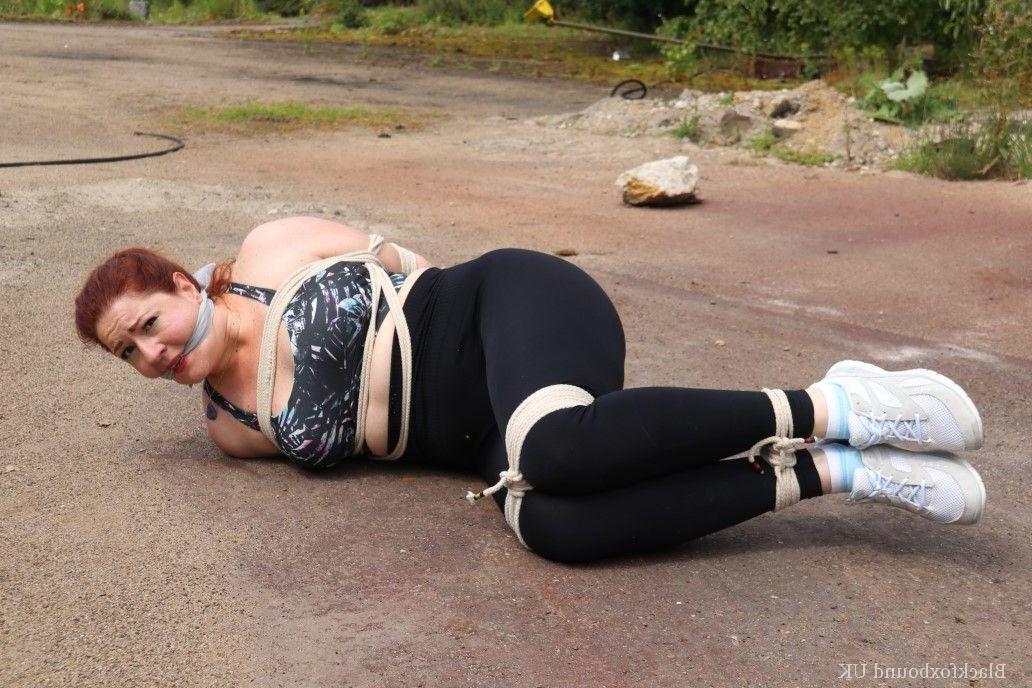 16P Redheaded girl Mada Rose is left on a paved lot while tied up