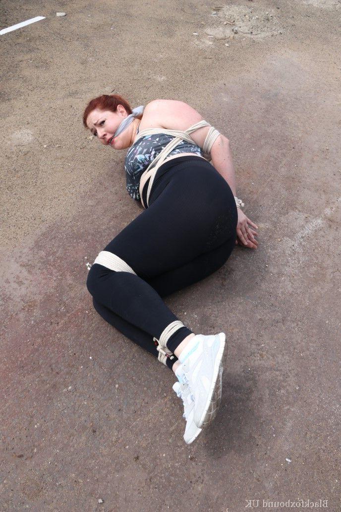 16P Redheaded girl Mada Rose is left on a paved lot while tied up