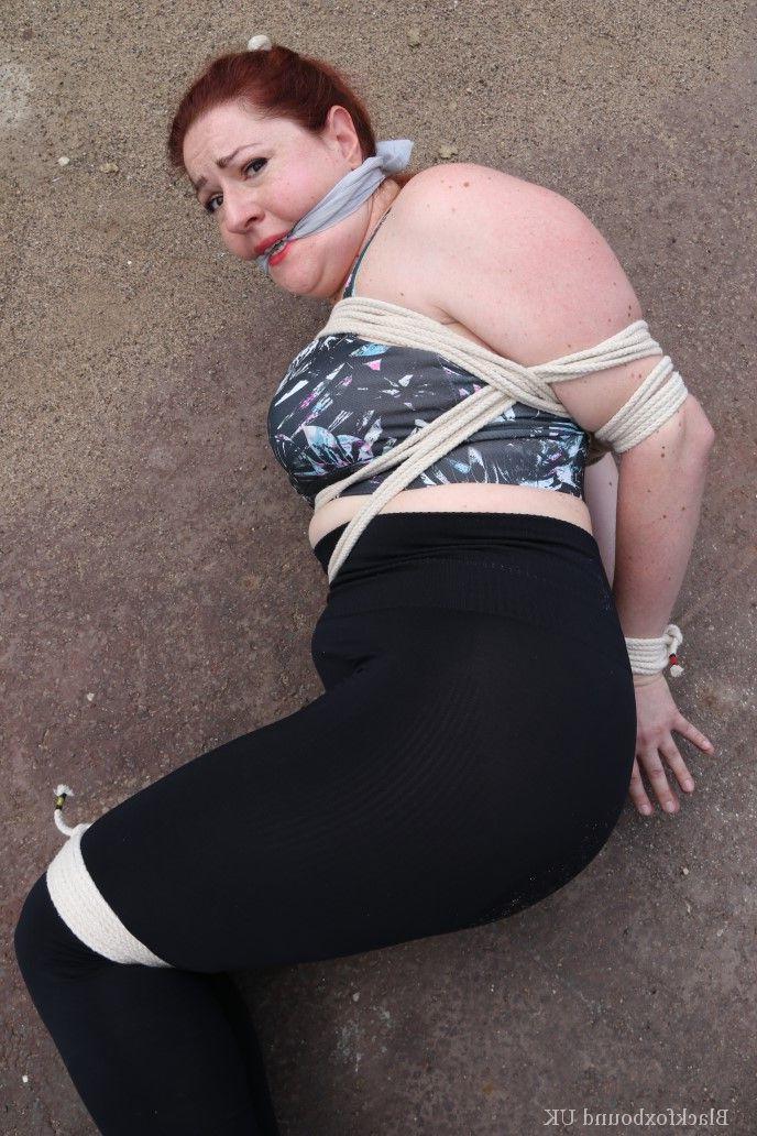16P Redheaded girl Mada Rose is left on a paved lot while tied up