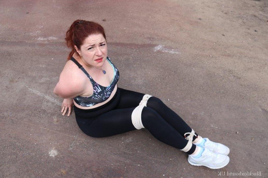16P Redheaded girl Mada Rose is left on a paved lot while tied up