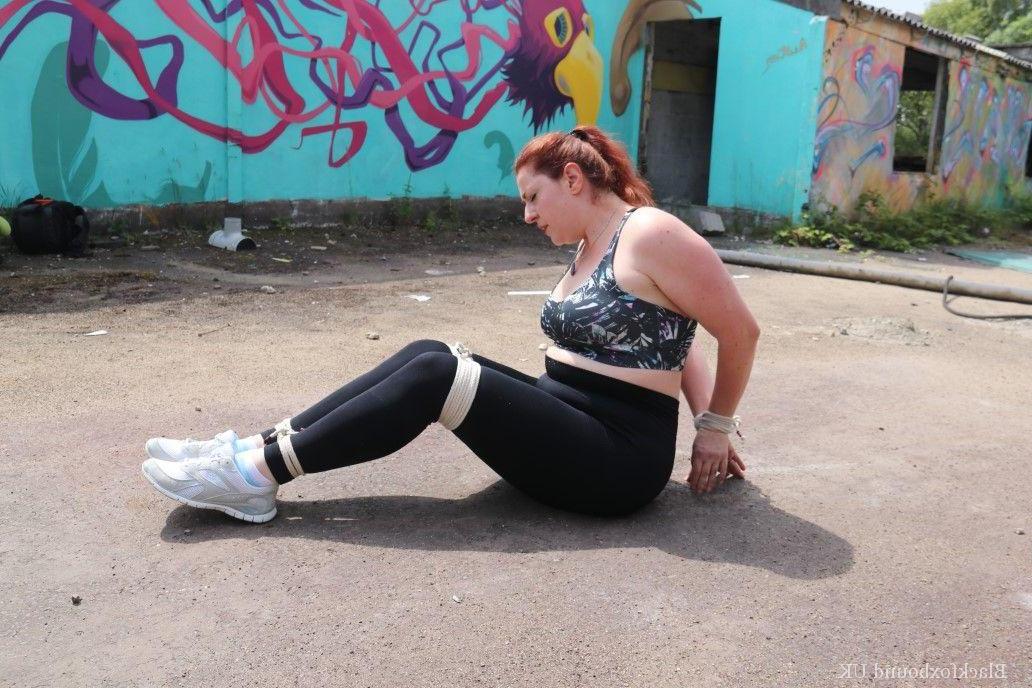 16P Redheaded girl Mada Rose is left on a paved lot while tied up