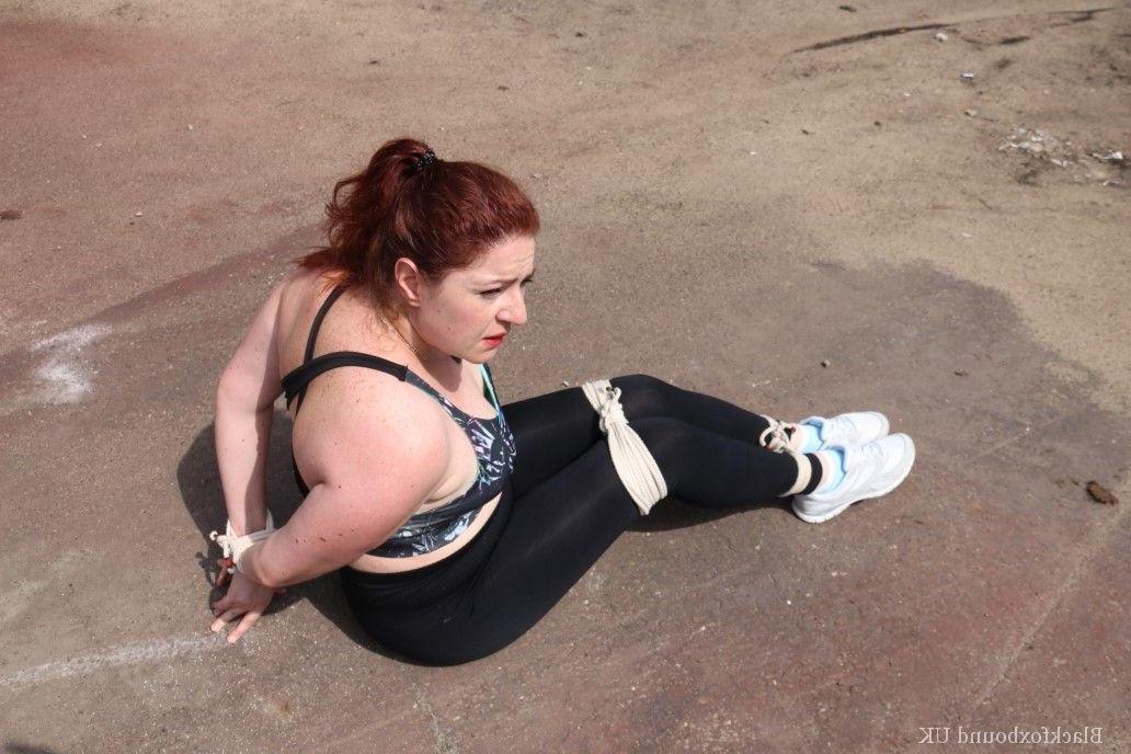16P Redheaded girl Mada Rose is left on a paved lot while tied up