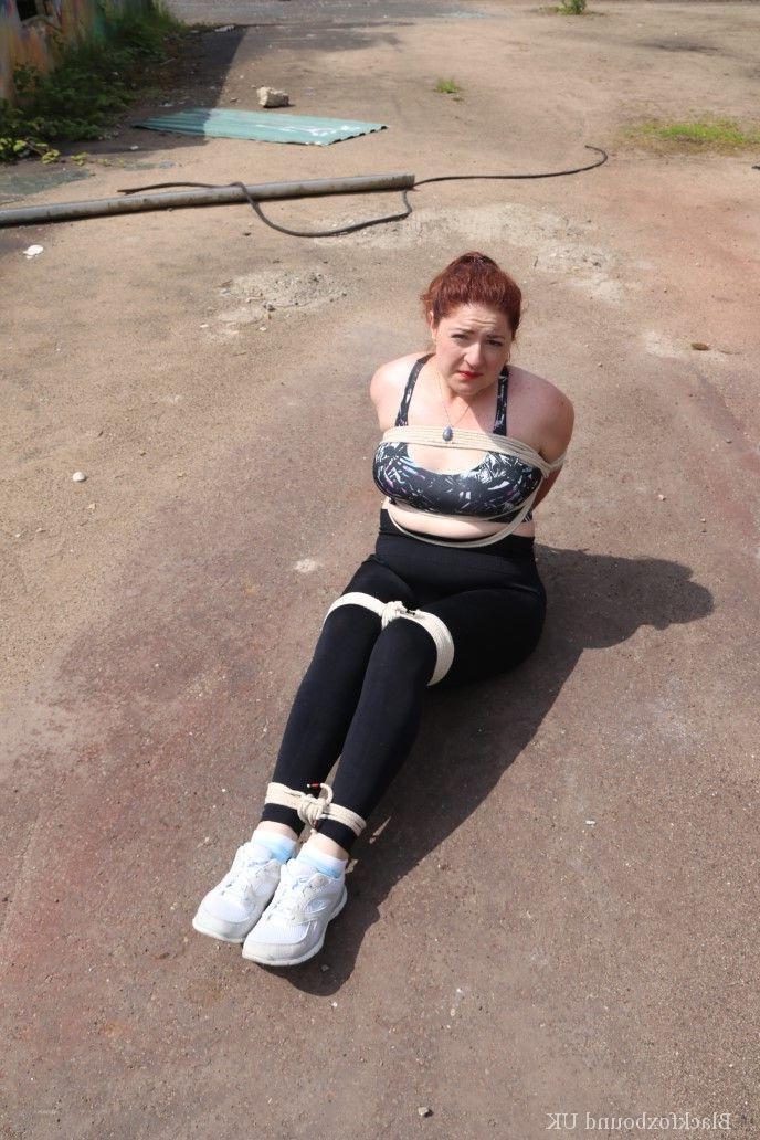 16P Redheaded girl Mada Rose is left on a paved lot while tied up
