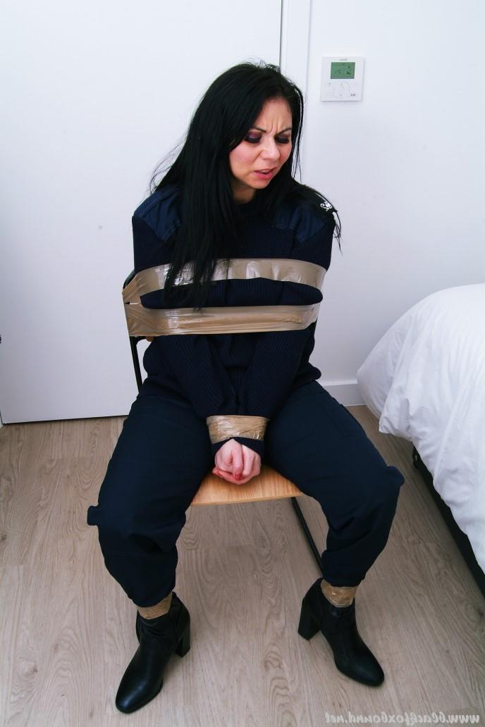 16P Mujer policía de cabello oscuro se encuentra atada a una silla con su uniforme