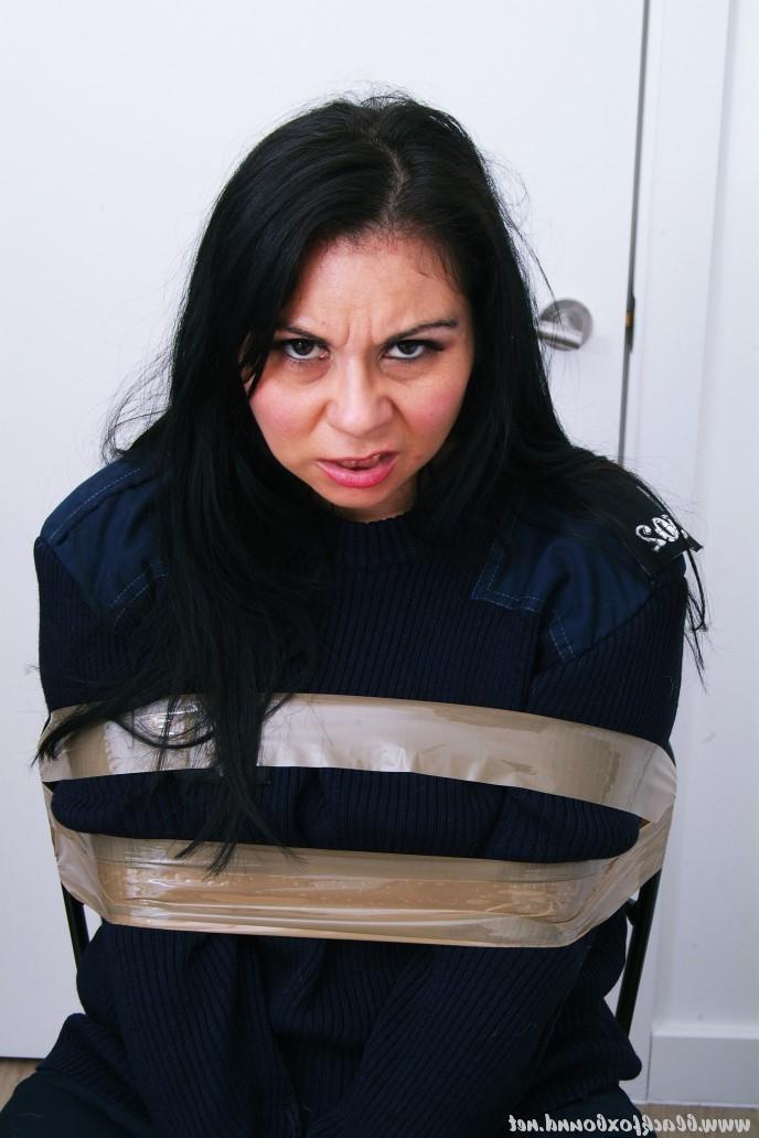 16P Mujer policía de cabello oscuro se encuentra atada a una silla con su uniforme