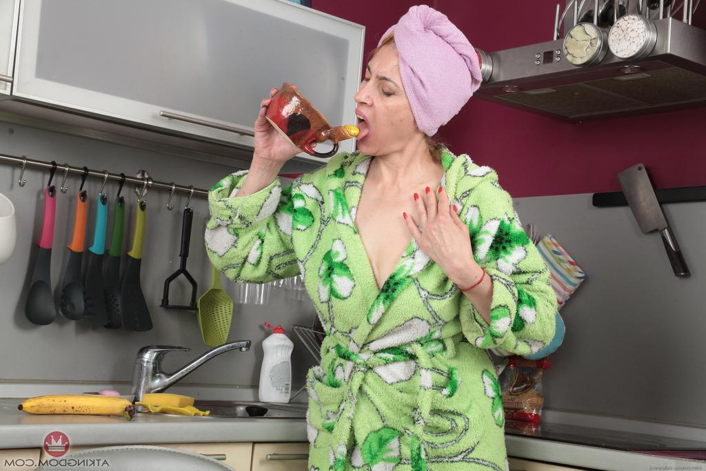 16P A dona de casa madura Karolina molha seu arbusto natural com uma xícara matinal na cozinha