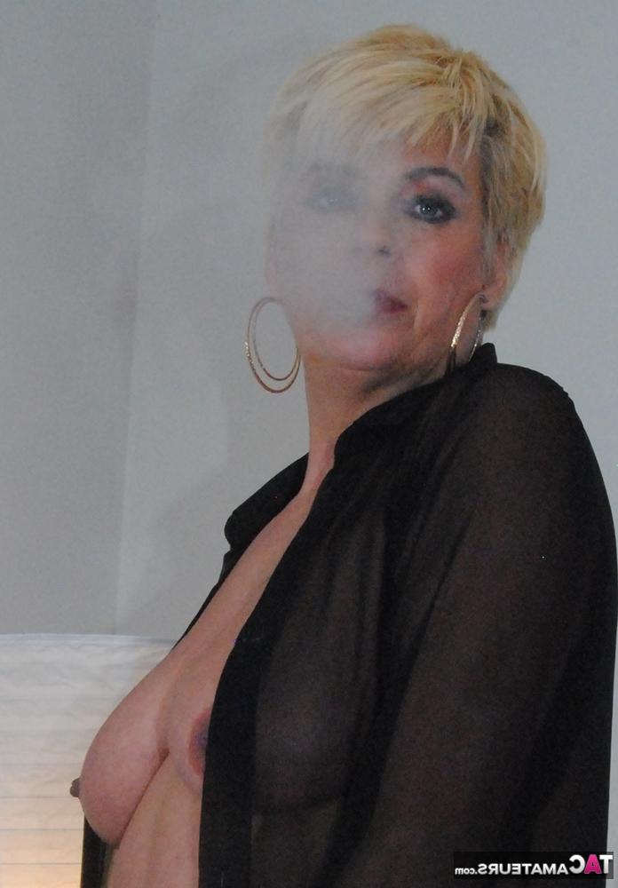 20P Older blonde Dimonty smokes while showing her boobs in a bedroom